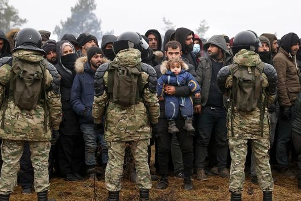 Migranten stehen an der belarussisch-polnischen Grenze vor belarussischen Soldaten.