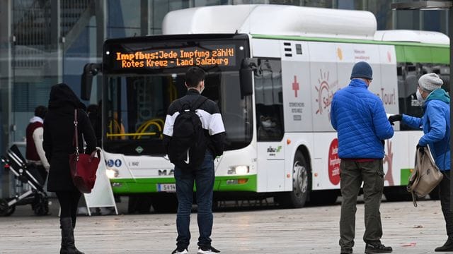 Menschen stehen in Salzburg in einer Warteschlange vor einem Impfbus.