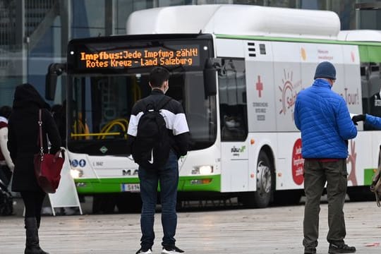 Menschen stehen in Salzburg in einer Warteschlange vor einem Impfbus.