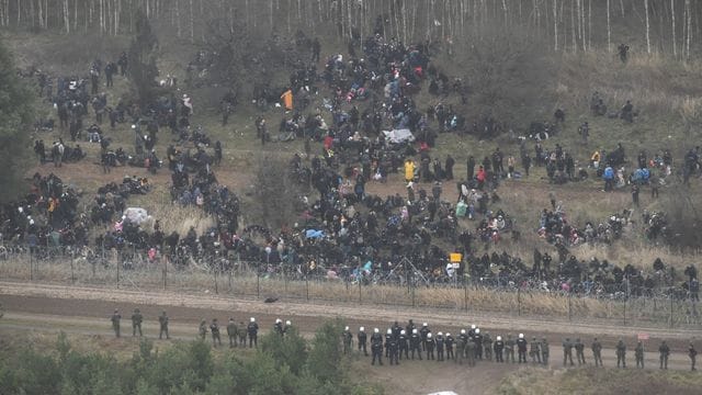 Menschen stehen hinter einem Grenzzaun in Belarus in der Nähe des polnisch-belarussischen Grenzübergangs in Kuznica.