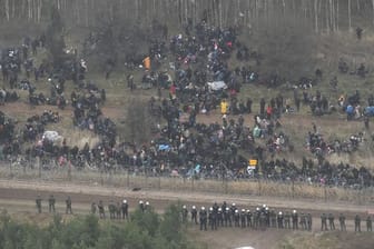 Menschen stehen hinter einem Grenzzaun in Belarus in der Nähe des polnisch-belarussischen Grenzübergangs in Kuznica.