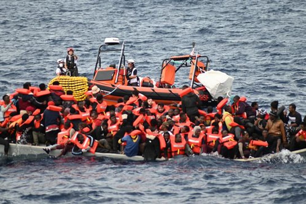 Ein Rettungsboot schwimmt hinter einem völlig überfüllten Flüchtlingsboot.