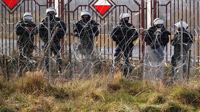 Polnische Sicherheitskräfte stehen an der Grenze hinter Stacheldraht.