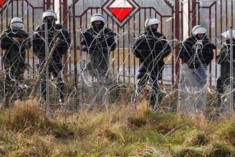 Polnische Sicherheitskräfte stehen an der Grenze hinter Stacheldraht.