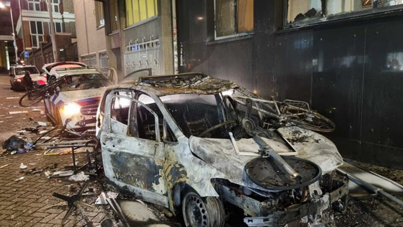 Ausgebrannte Autos, darunter auch Polizeifahrzeuge, stehen auf einer Straße in Rotterdam.