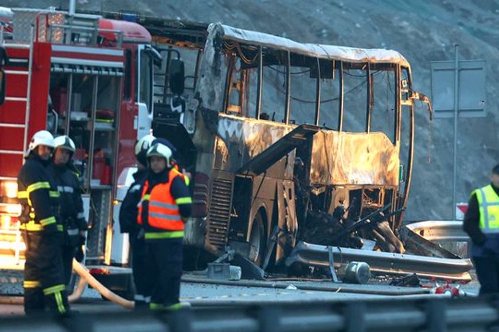 Rettungskräfte der Feuerwehr an der Unfallstelle neben dem ausgebrannten Bus.