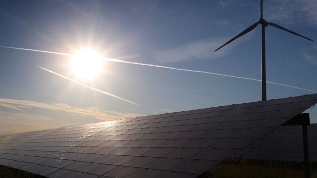 Ein Windrad steht hinter den Solarzellen einer Solarkraftanlage im Sonnenschein. Ein Windrad steht hinter den Solarzellen einer Solarkraftanlage im Sonnenschein.