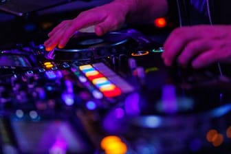 Die Hände eines DJ bedienen ein Mischpult in einem Club.