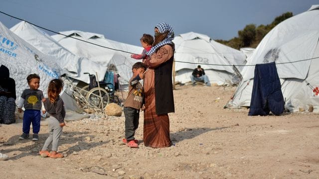 Eine Frau steht mit einem Baby im Arm und drei kleinen Kindern im Flüchtlingslager Kara Tepe in der Nähe von Mytilini auf Lesbos zwischen Zelten.