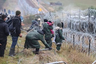 Getrennt durch Stacheldraht: Migranten stehen an der Grenze auf der belarussischen Seite - auf der polnischen stehen Sicherheitskräfte.