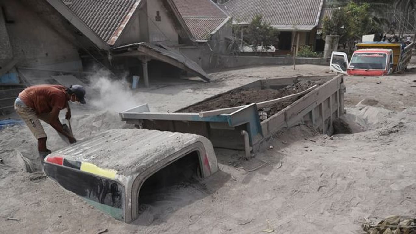 Ein Mann inspiziert einen Lastwagen, der nach dem Ausbruch des Mount Semeru unter Vulkanasche begraben wurde.