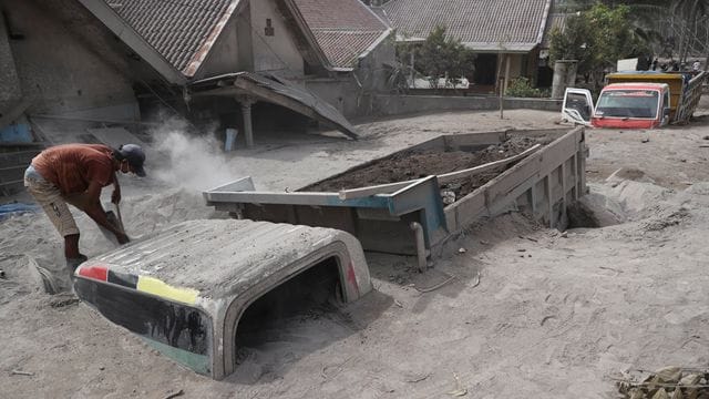 Ein Mann inspiziert einen Lastwagen, der nach dem Ausbruch des Mount Semeru unter Vulkanasche begraben wurde. Ein Mann inspiziert einen Lastwagen, der nach dem Ausbruch des Mount Semeru unter Vulkanasche begraben wurde.