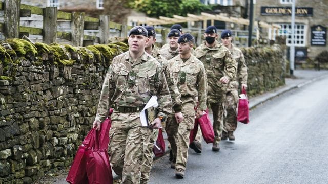 Angehörige der Streitkräfte tragen Versorgungspakete, um sie an Betroffene im britischen St.