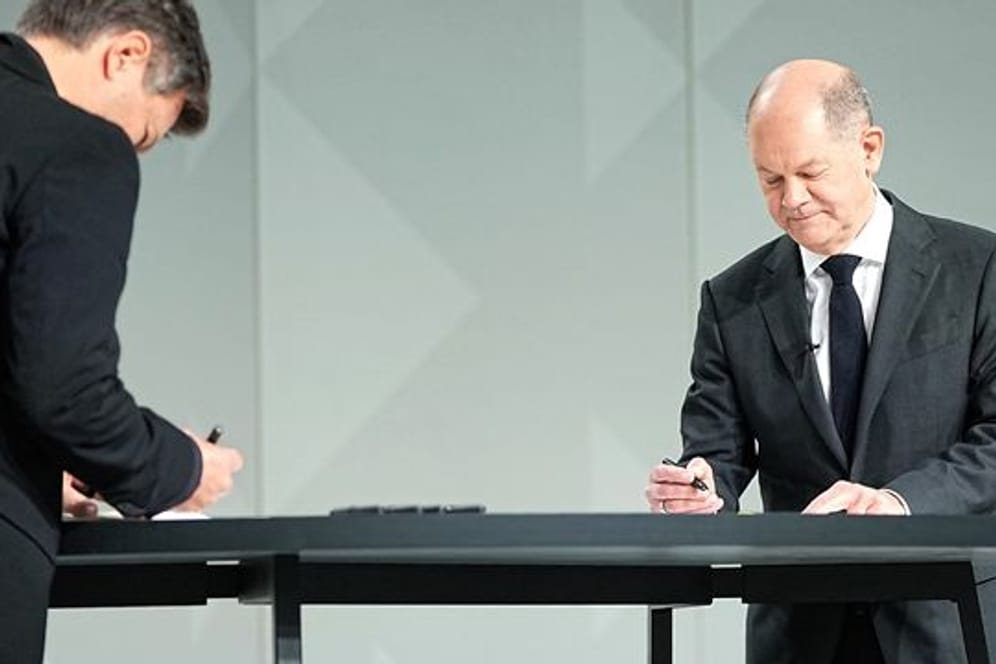 Der Grünen-Vorsitzende Robert Habeck (l) und der neue Kanzler Olaf Scholz (SPD) setzen ihre Unterschriften unter das Dokument.