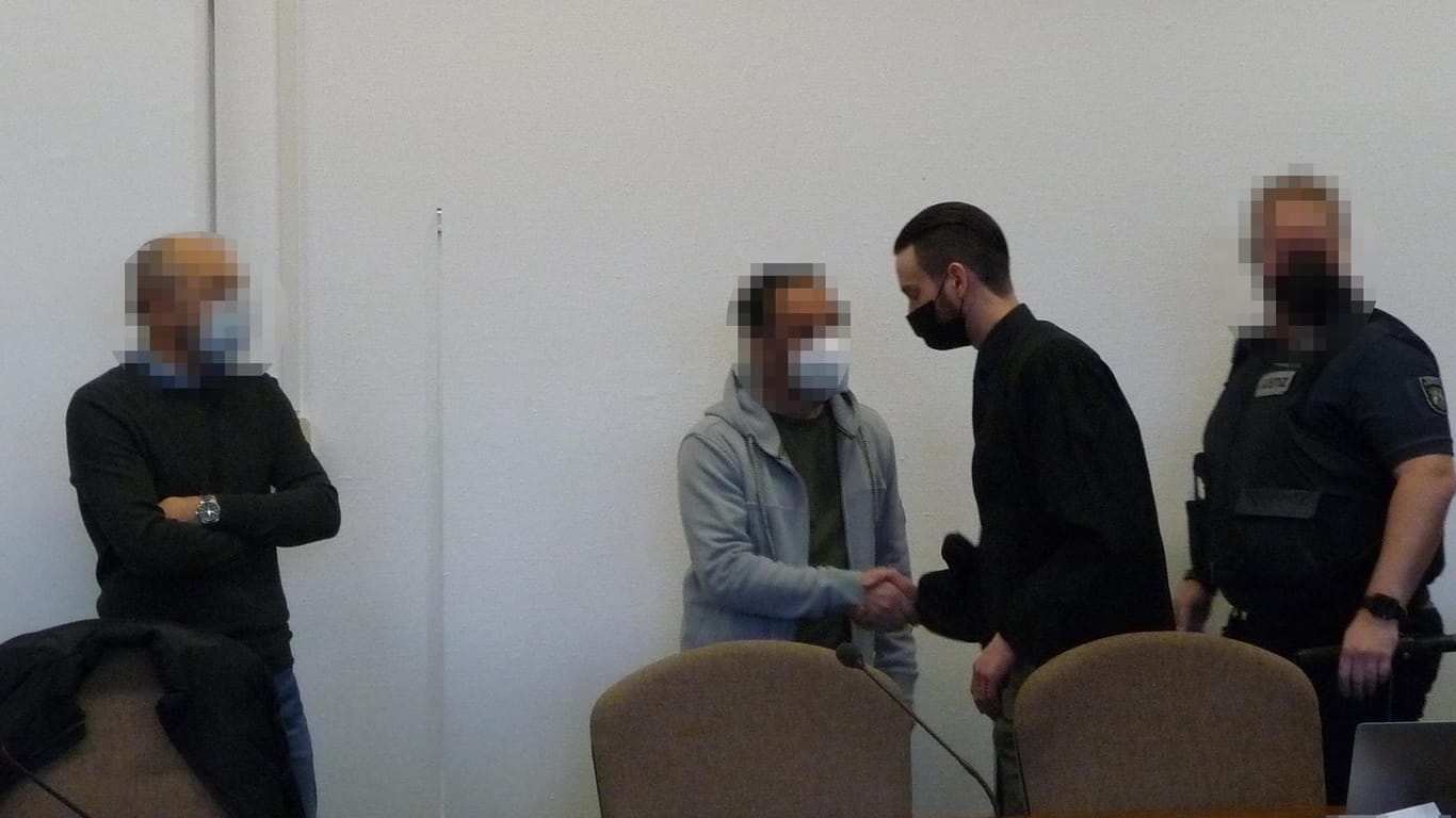Einer der Angeklagten (zweiter v. l.) wird aus der Haft vorgeführt und begrüßt seinen Verteidiger, Maximilian Eßer.
