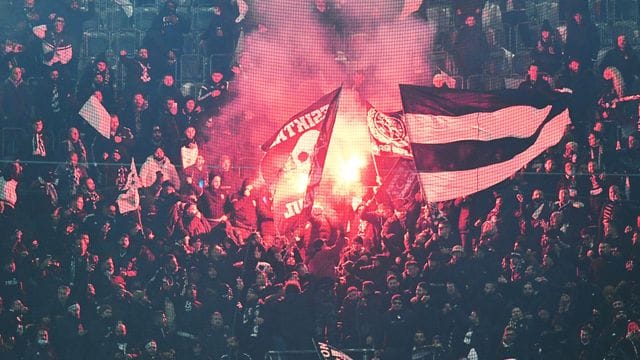 Fans von Besiktas stehen hinter einem Zaun auf der Tribüne und zünden Pyrotechnik.