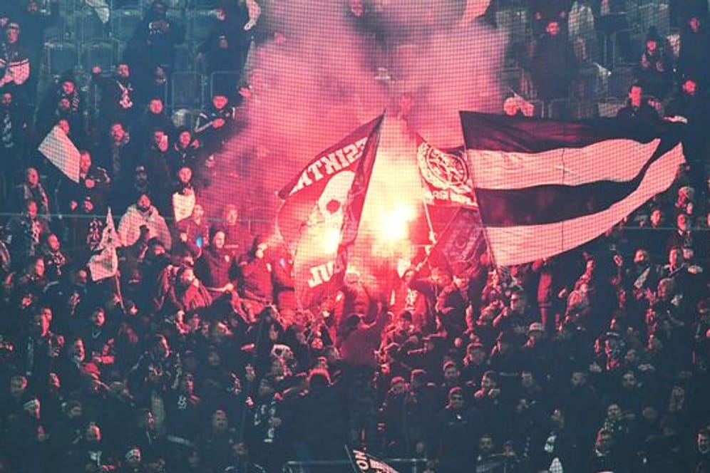 Fans von Besiktas stehen hinter einem Zaun auf der Tribüne und zünden Pyrotechnik.