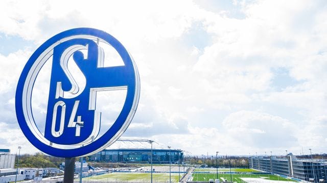 Im Vordergrund dreht sich das Logo des FC Schalke 04 - der Zweitligist hat Sparpläne.