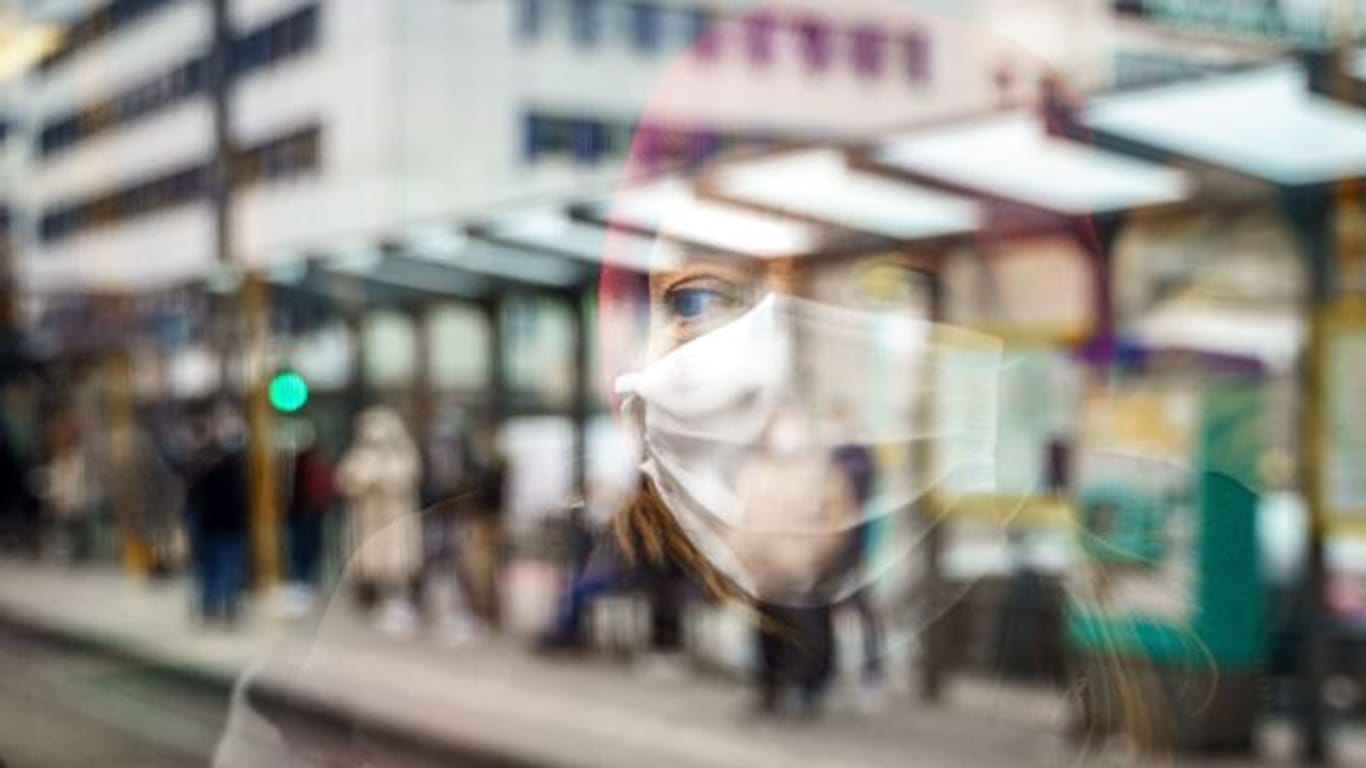 Eine Frau mit Mund-Nasen-Schutz spiegelt sich im Fenster einer Straßenbahn an der Konstablerwache in der Frankfurter Innenstadt.