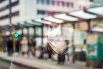 Eine Frau mit Mund-Nasen-Schutz spiegelt sich im Fenster einer Straßenbahn an der Konstablerwache in der Frankfurter Innenstadt.