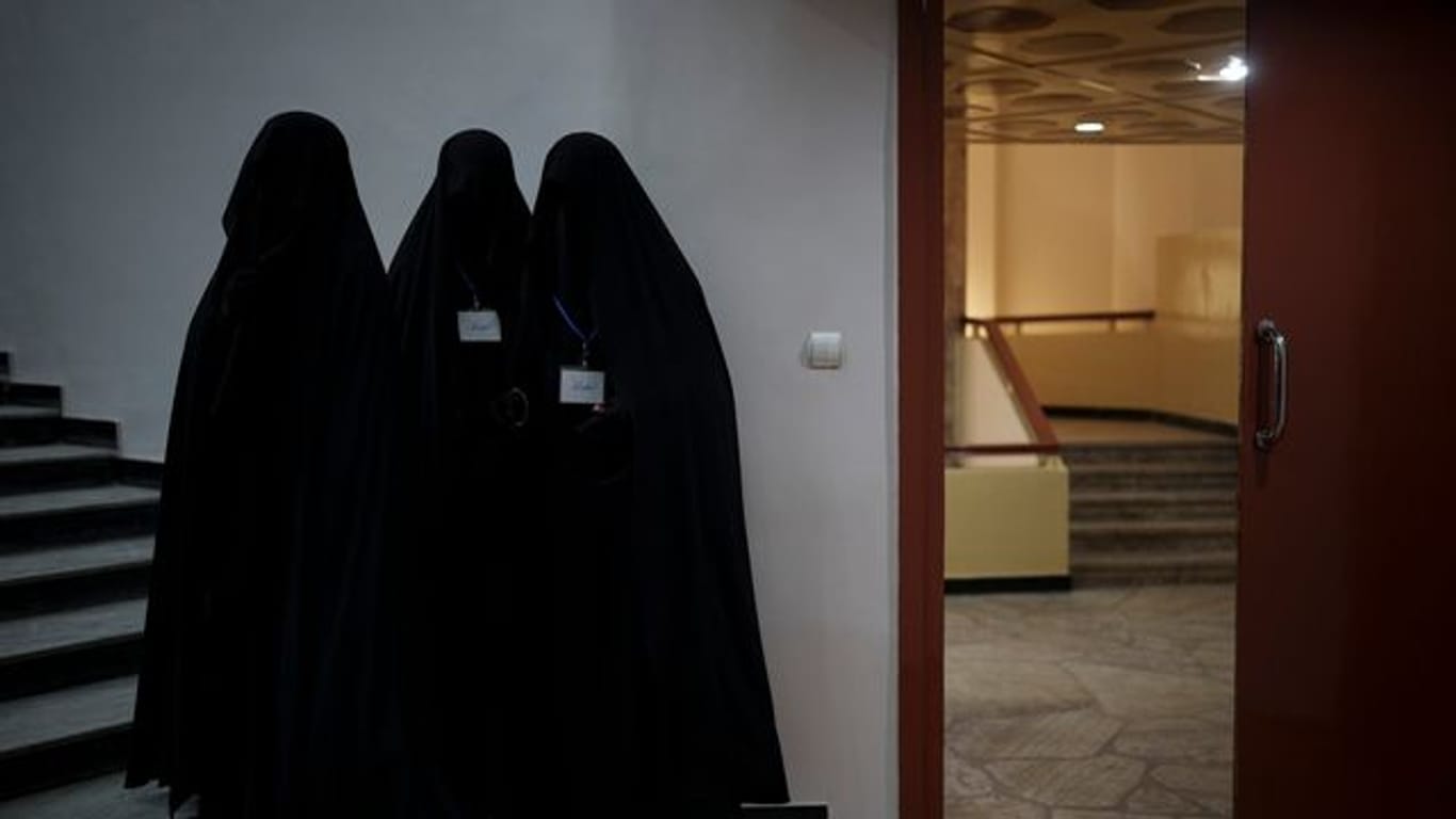 Drei in schwarzen Burkas gehüllte Frauen stehen vor einem Hörsaal der Universität in Kabul.