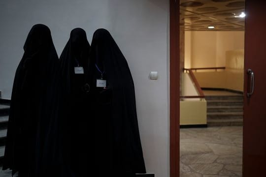 Drei in schwarzen Burkas gehüllte Frauen stehen vor einem Hörsaal der Universität in Kabul.