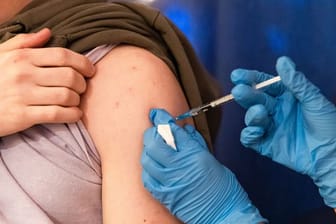 Einer Person wird der Corona-Impfstoff in den Oberarm verabreicht.