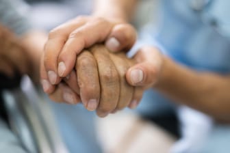 Ein Pfleger hält die Hand eines Patienten (Symbolbild): Frankreichs ältester Mann erkrankte schwer an Corona.