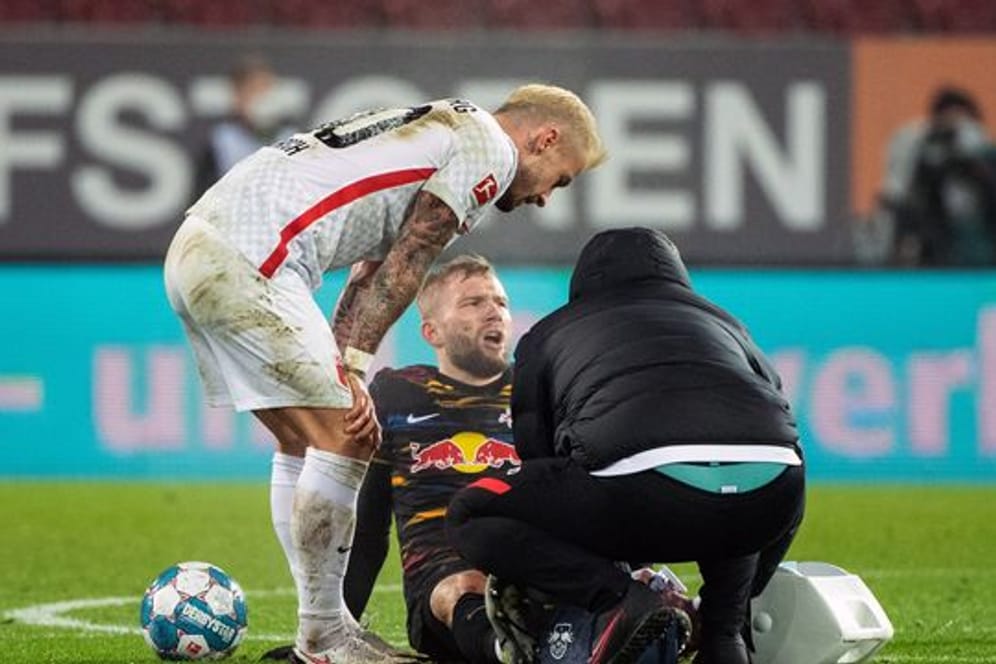 Konrad Laimer von RB Leipzig (M) sitzt verletzt auf dem Spielfeld und wird behandelt.