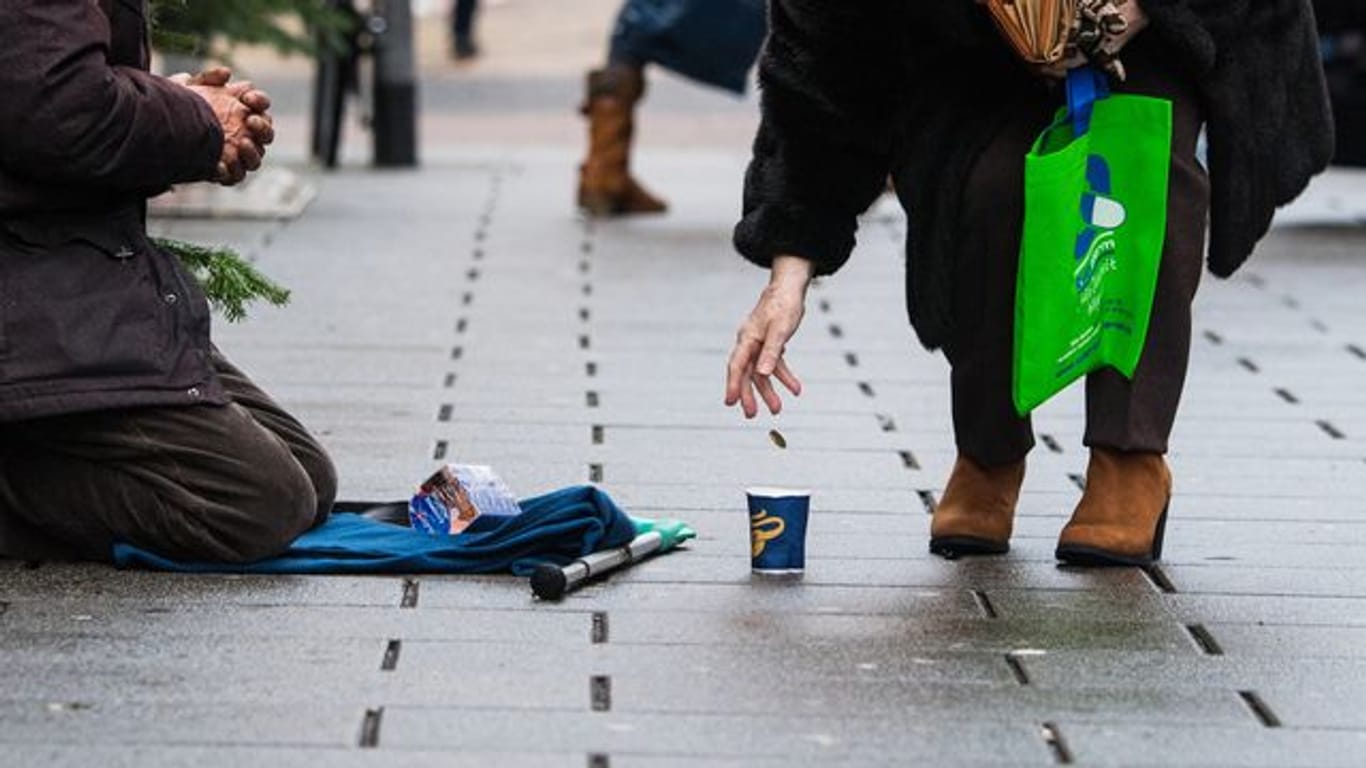 Eine Frau wirft einem Bettler in einer Einkaufsstraße ein Geldstück in einen Becher.