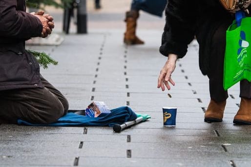 Eine Frau wirft einem Bettler in einer Einkaufsstraße ein Geldstück in einen Becher.