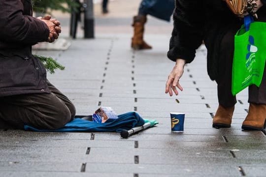 Eine Frau wirft einem Bettler in einer Einkaufsstraße ein Geldstück in einen Becher.