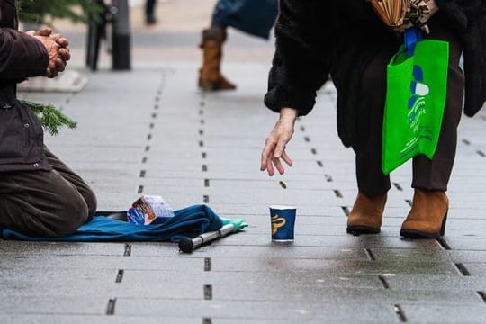 Eine Frau wirft einem Bettler in einer Einkaufsstraße ein Geldstück in einen Becher.