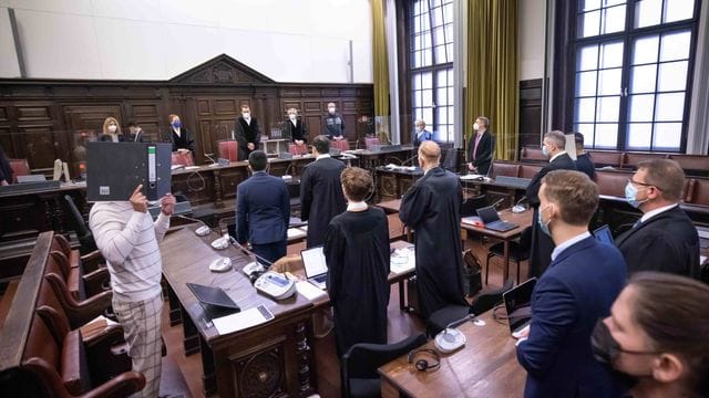 Der Hauptangeklagte (l, in Untersuchungshaft), sowie weitere Angeklagte, Anwälte und Prozessbeteiligte, stehen vor Beginn des Prozesses im Gerichtssaal. Der Hauptangeklagte (l, in Untersuchungshaft), sowie weitere Angeklagte, Anwälte und Prozessbeteiligte, stehen vor Beginn des Prozesses im Gerichtssaal.