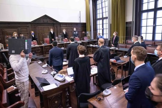 Der Hauptangeklagte (l, in Untersuchungshaft), sowie weitere Angeklagte, Anwälte und Prozessbeteiligte, stehen vor Beginn des Prozesses im Gerichtssaal.