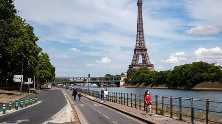 Menschen spazieren an der Seine neben dem Eiffelturm.