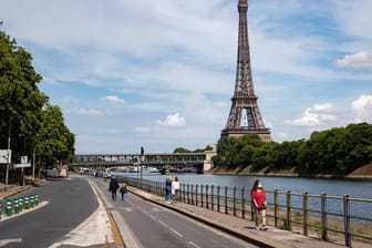 Menschen spazieren an der Seine neben dem Eiffelturm.