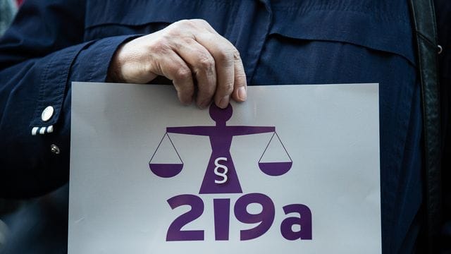 Eine Frau hält bei einer Kundgebung einen Zettel mit der Aufschrift "219a nicht zeitgemäß!". Eine Frau hält bei einer Kundgebung einen Zettel mit der Aufschrift "219a nicht zeitgemäß!".