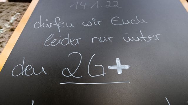 Auf einem Schild wird vor einem Cafe auf die 2G-plus-Regel hingewiesen.