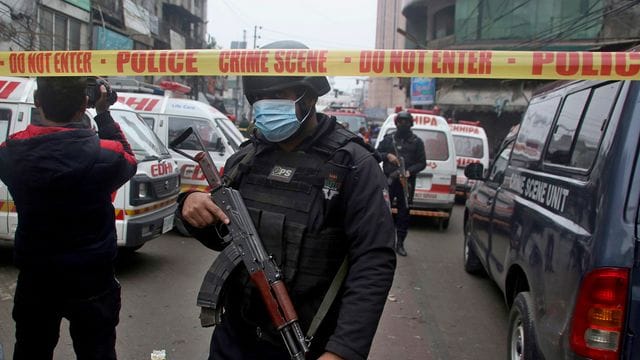 Polizisten stehen am Anschlagsort in Lahore, während Krankenwagen darauf warten Verletzte abzutransportieren.