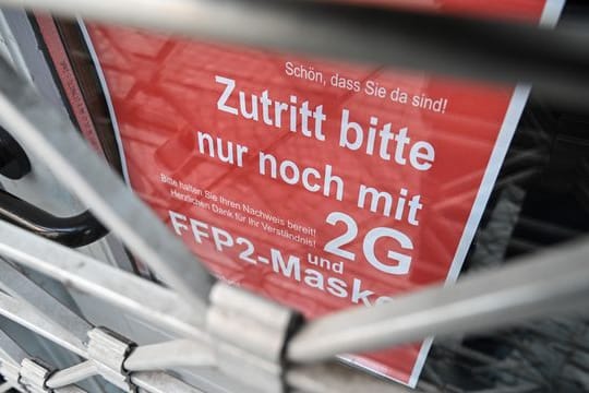 Ein Schild weist am Eingang eines Ladens in der Innenstadt auf die Maskenpflicht und die 2G-Regel hin.