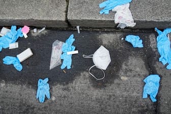 Einmalhandschuhe, FFP2-Maske und benutzte Corona-Antigen-Testkits liegen auf der Straße vor einem Corona-Testzentrum.