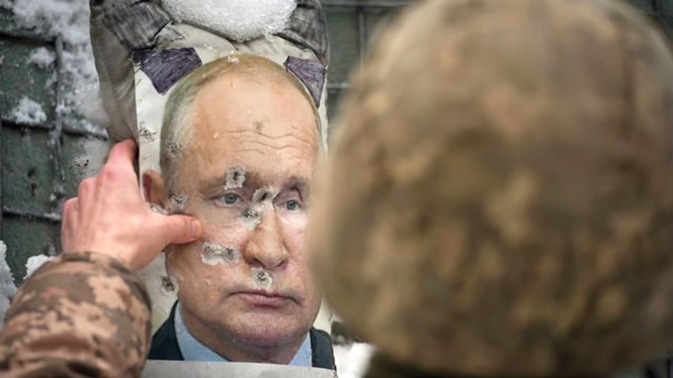 Ein ukrainischer Soldat justiert ein von Kugeln durchlöchertes Bild des russischen Präsidenten Putin.