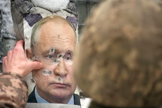 Ein ukrainischer Soldat justiert ein von Kugeln durchlöchertes Bild des russischen Präsidenten Putin.