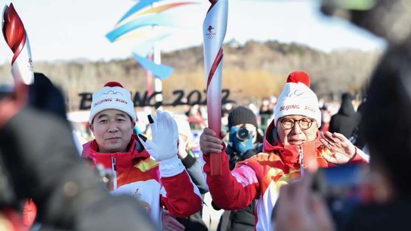 Der erste Fackelträger Luo Zhihan (r), ehemaliger Eisschnelllauf-Weltmeister, übergibt die Fackel an den chinesischen Astronauten Jing Haipeng.