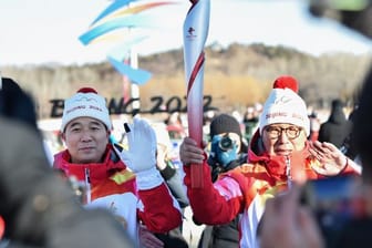 Der erste Fackelträger Luo Zhihan (r), ehemaliger Eisschnelllauf-Weltmeister, übergibt die Fackel an den chinesischen Astronauten Jing Haipeng.