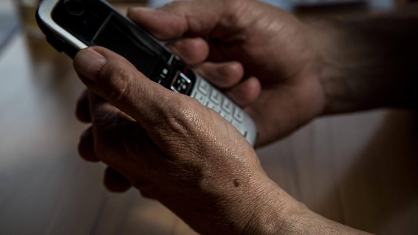 Die Hand eines älteren Menschen hält ein Telefon (Symbolbild): Immer mehr Senioren in Frankfurt werden Opfer von Schockanrufen.