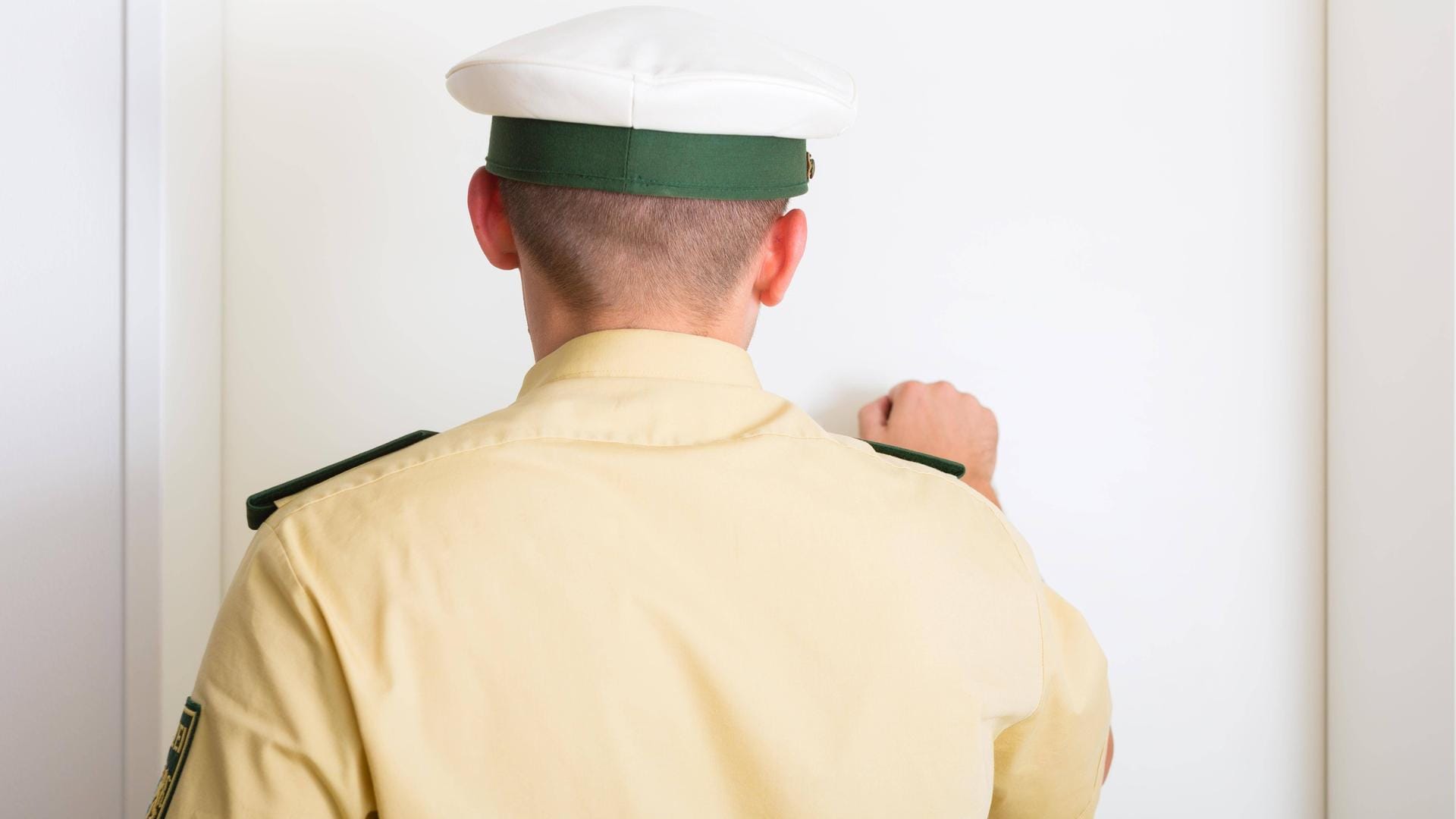 Ein Mann in einer Polizei-Uniform klopf an eine Tür (Symbolbild): Die Betrüger gaben an, Beute zurückzubringen.
