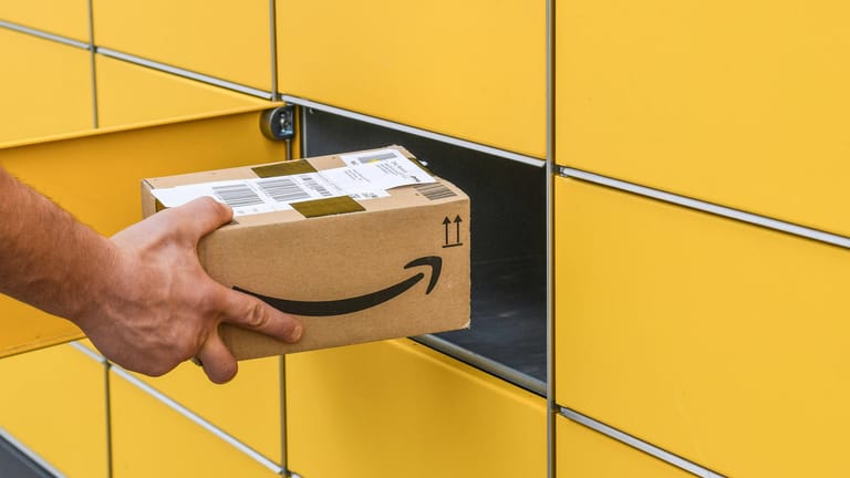 Ein Mann steckt ein Paket ein Amazon-Paket in eine Packstation (Symbolbild): Der Onlinehändler erhöht in den USA seine Preise für seinen Prime-Dienst.