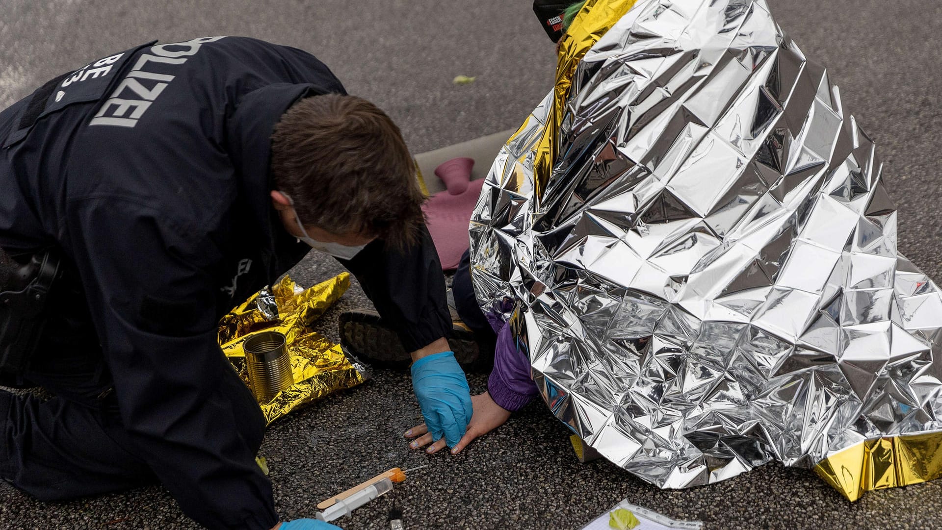 Ein Polizist löst den Klebstoff, mit dem sich ein Aktivist festgeklebt hat, von der Hand und der Fahrbahn: Die Proteste an Zufahrten zu Autobahnen hatten vergangene Woche begonnen.